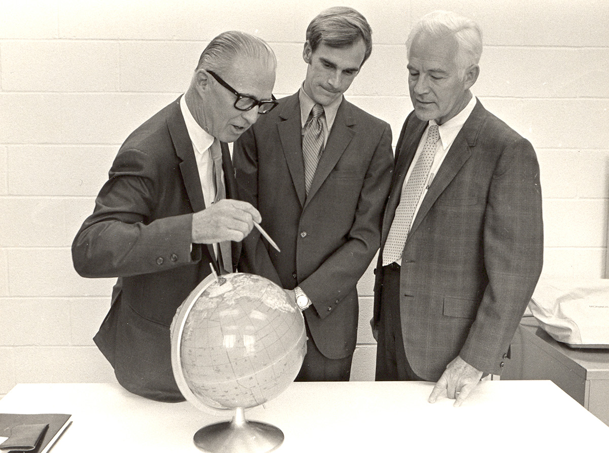 Three men examine a globe